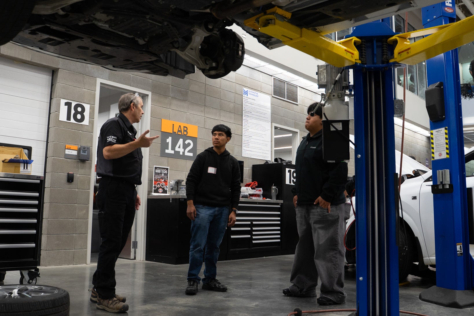 Instructor talks with students beneath a raised vehicle.