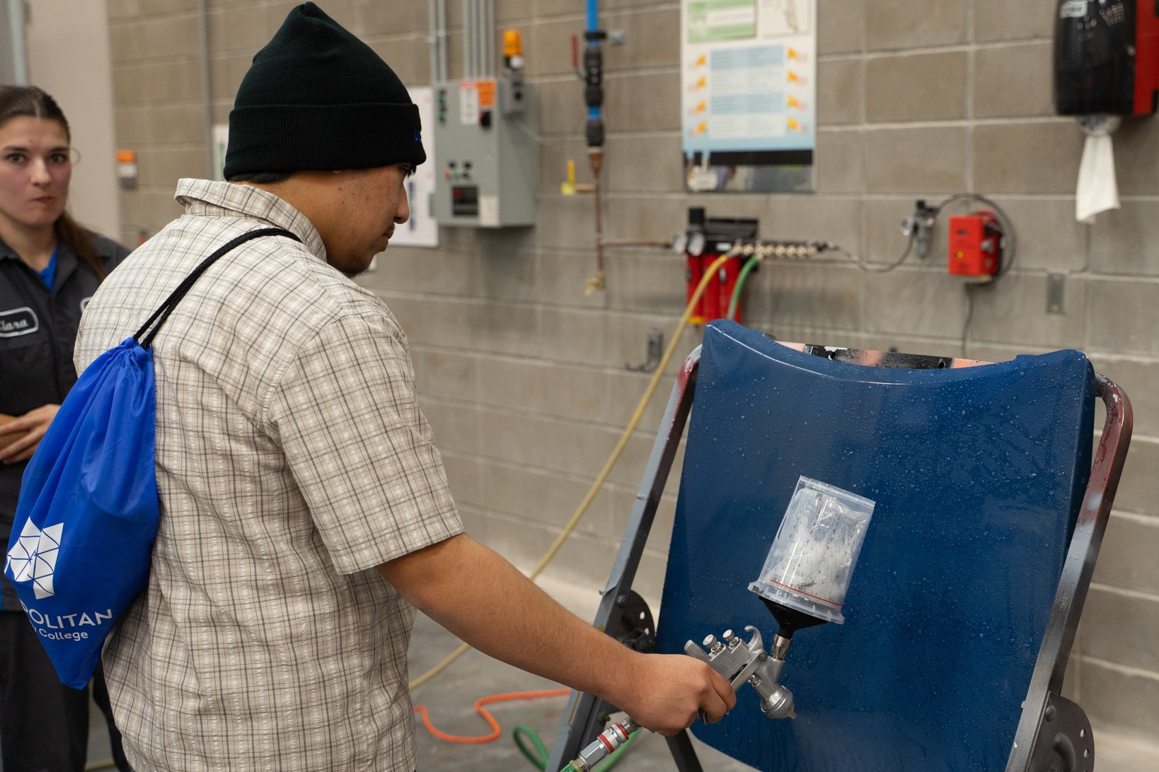 Student practices using a paint spray gun on a car panel.