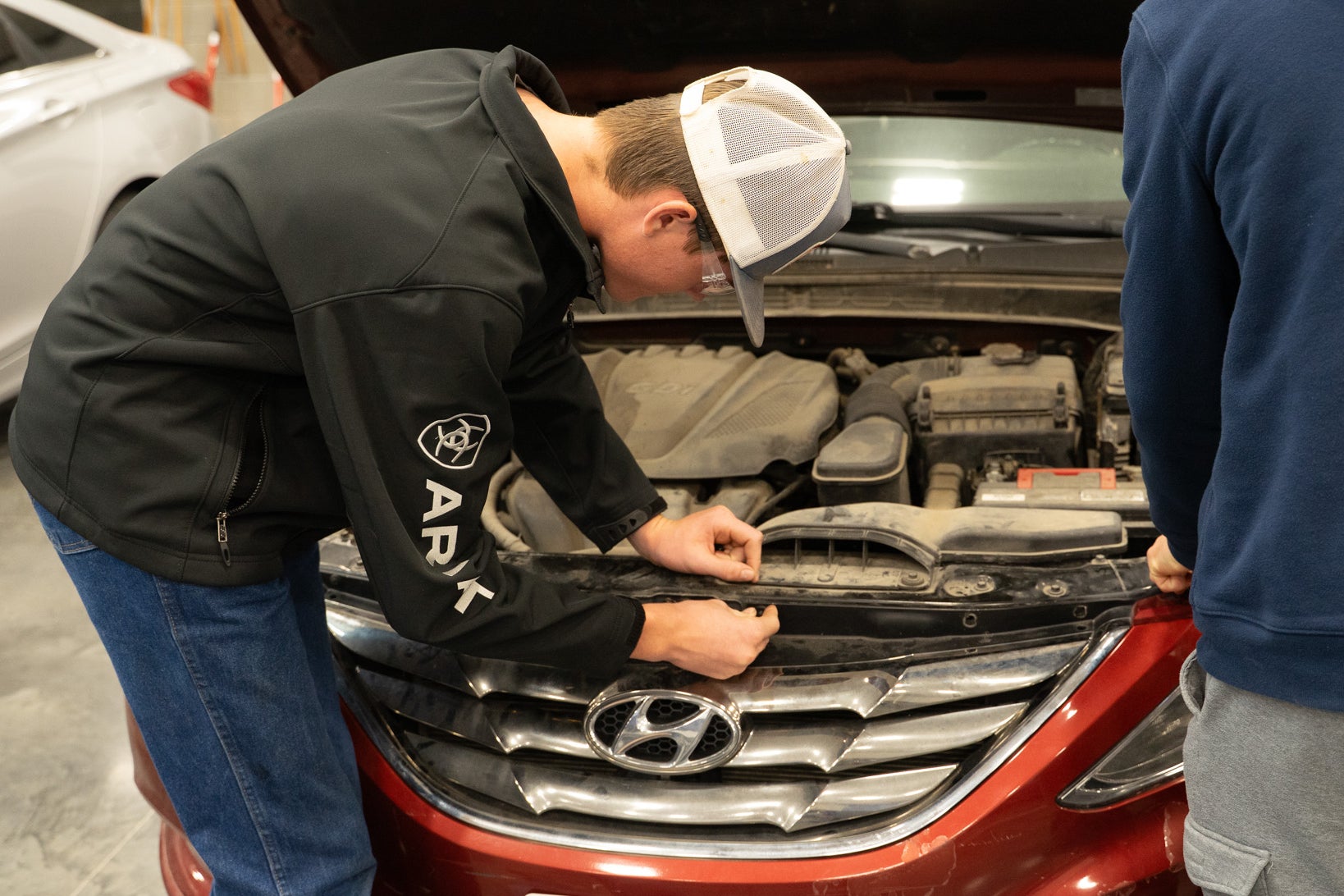 Student examines a car engine with its hood open.