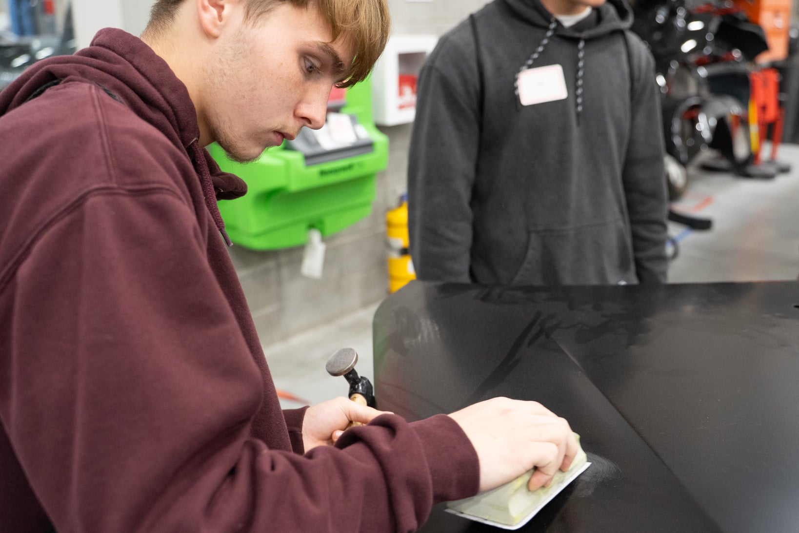 Student sands a car panel during a hands-on activity.