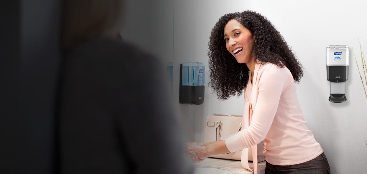 Women in restroom with Purell hand soap dispenser and Purell hand sanitizer dispenser