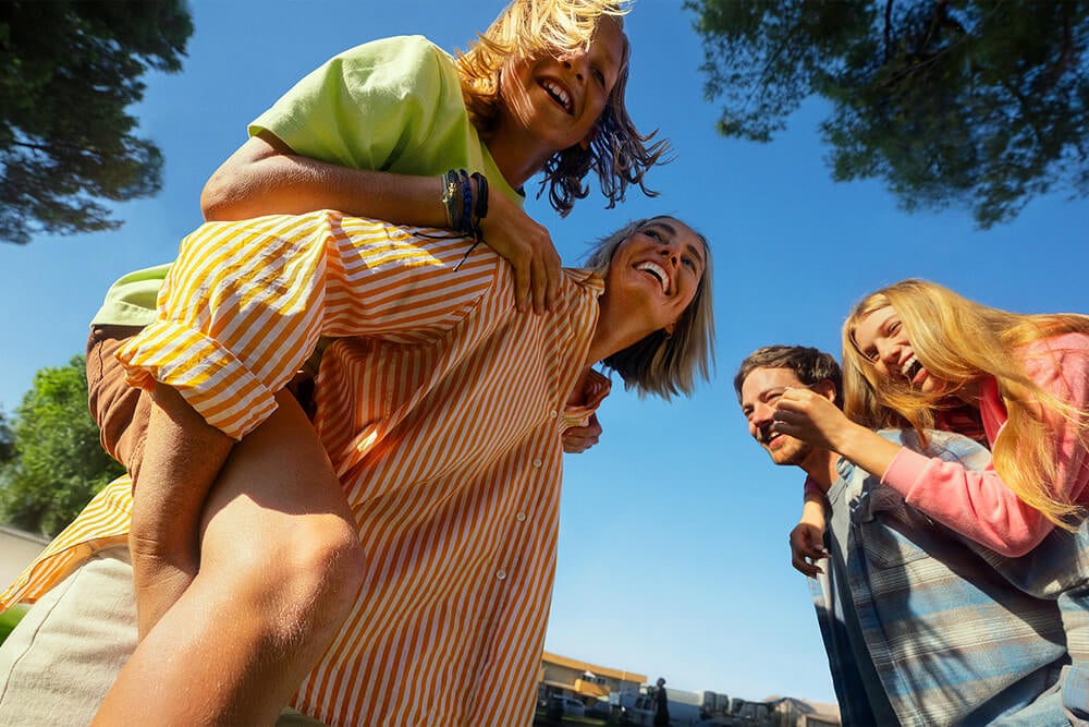 Parents carrying their daughters piggyback as they laugh in the sunshine.