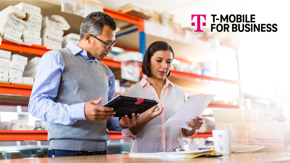 Two T-Mobile for Business partners reviewing print-out and tablet in stockroom.