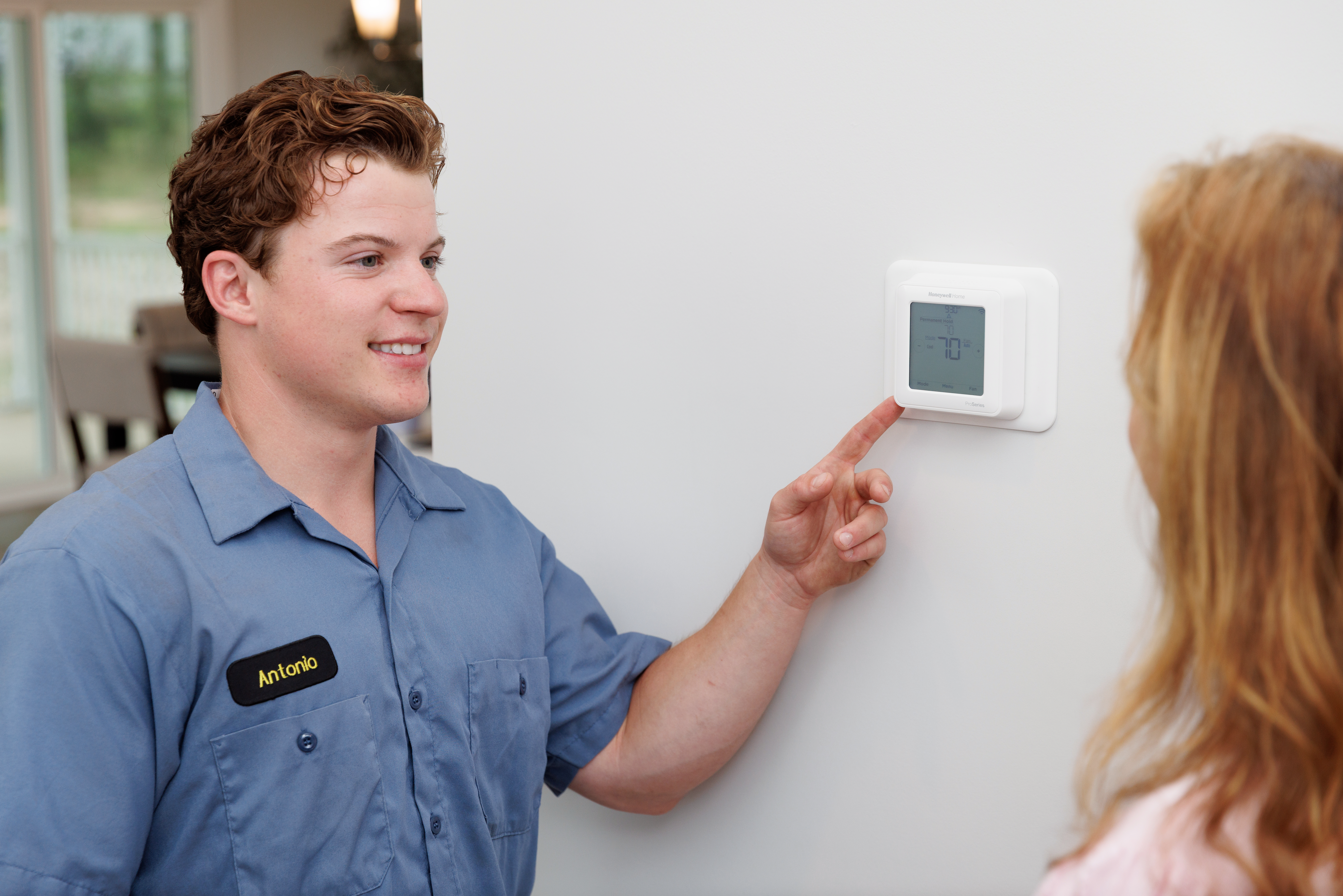 All American HVAC technician adjusting heat on thermostat