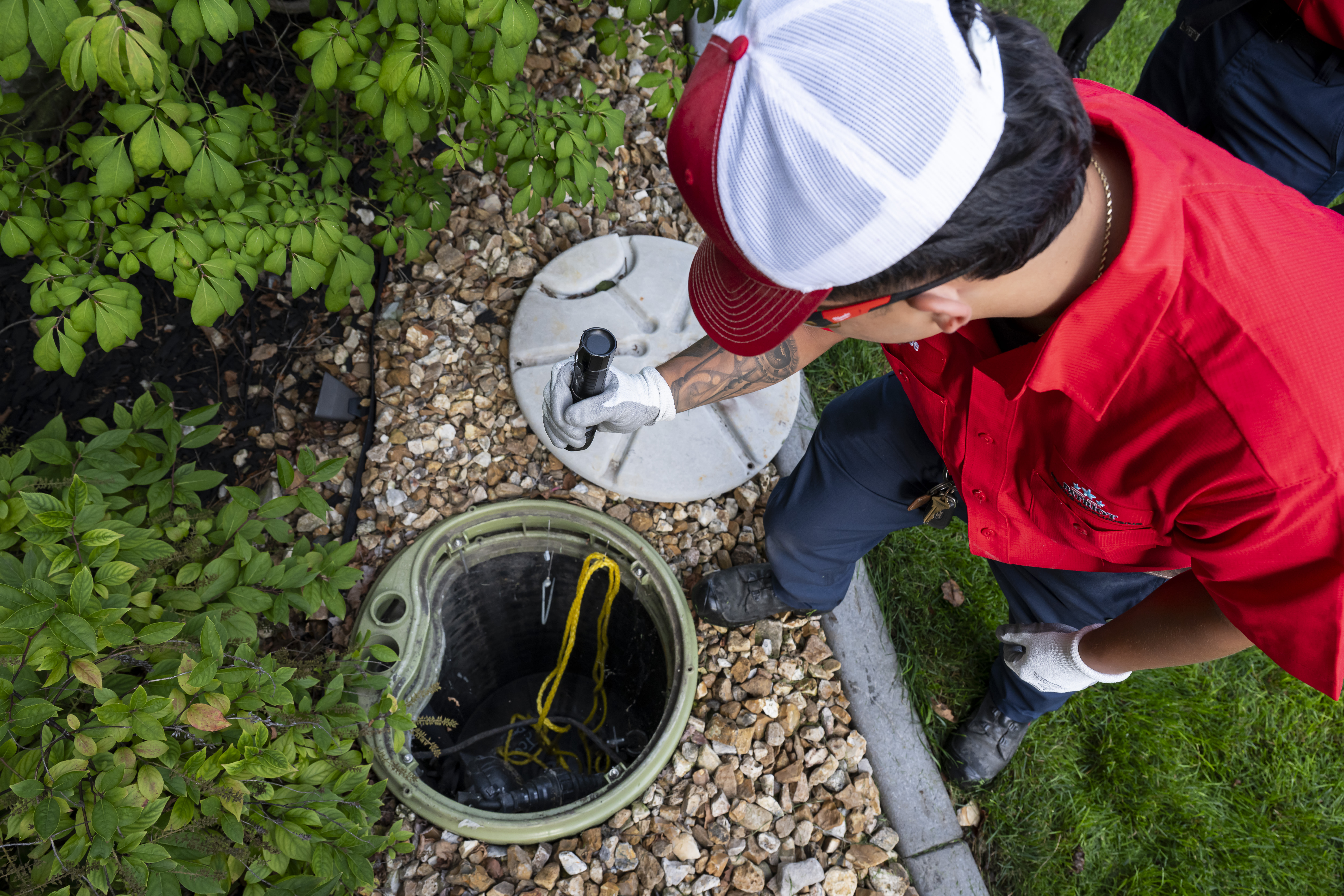 Patriot Heating & AC plumber working at an open access pit in a yard