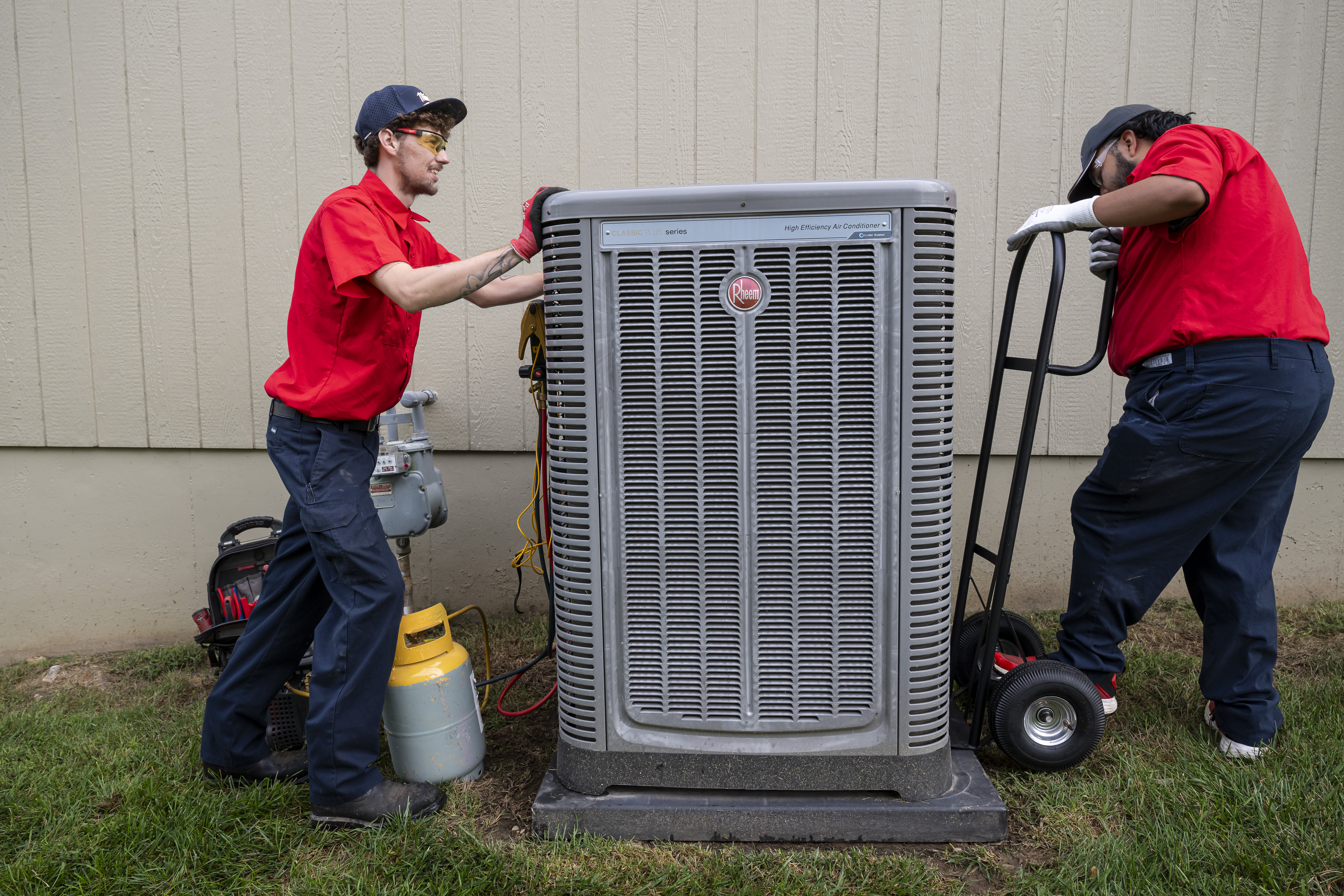 Two Patriot Heating & AC technicians moving a new air conditioning unit into place