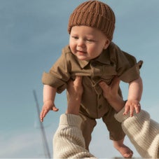 baby boy being held up wearing brown beanie and jumpsuit