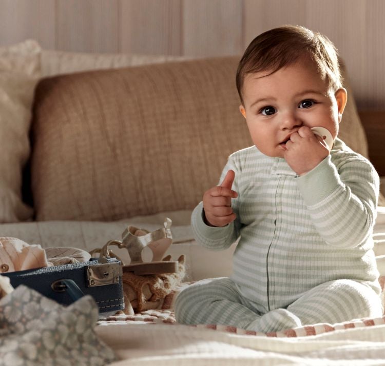 baby with a pacifier sitting on a bed by luggage