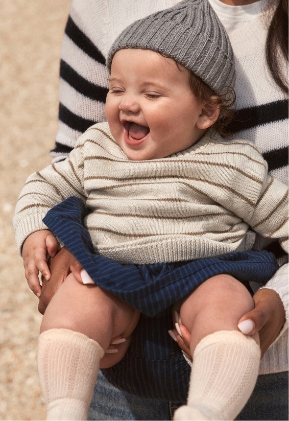laughing baby girl in grey beanie, striped sweater and a dress