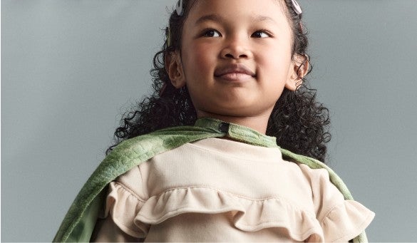 girl wearing a green cape and cream colored shirt