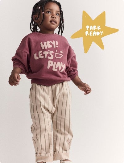 little boy in striped pants and shorts that say "Hey! Let's play!"