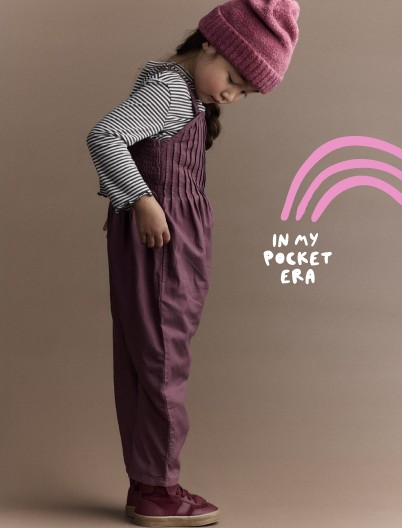 Toddler girl in purple pleated overalls and a beanie