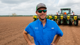 Texas cotton farmer Philip Marek stand in a field in front of his planter upgraded with Precision Planting.