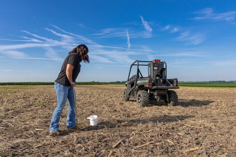 A farmer pressing a probe into the ground, with GeoPress in the background
