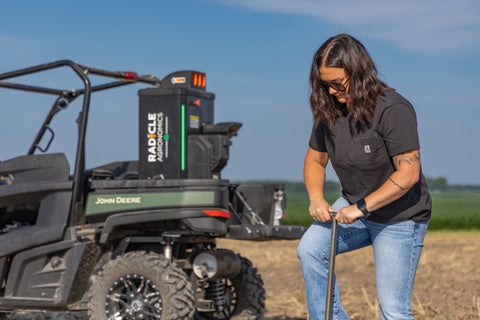 Woman pushing a probe into the ground, GeoPress Ultra on UTV in the background