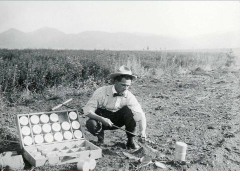 An agronomist in a black and white photo collects soil samples in the early 1900s.