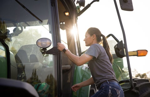 Woman farmer opening door and walking into a tractor