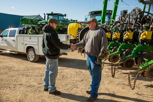 Premier Dealer and a farmer shaking hands in front of a John Deere planter and a pickup truck.