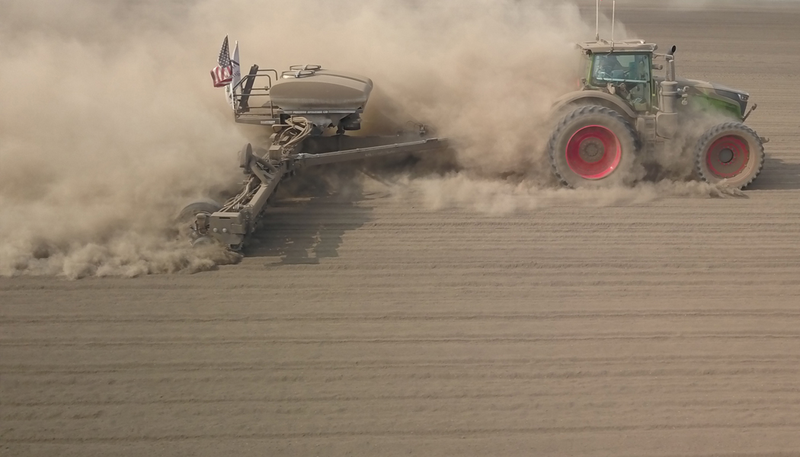 A planter moving across a dusty field.