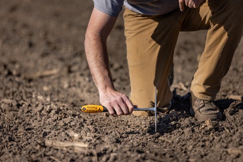 Farmer using a furrow finder to check the seed trench behind the planter. 