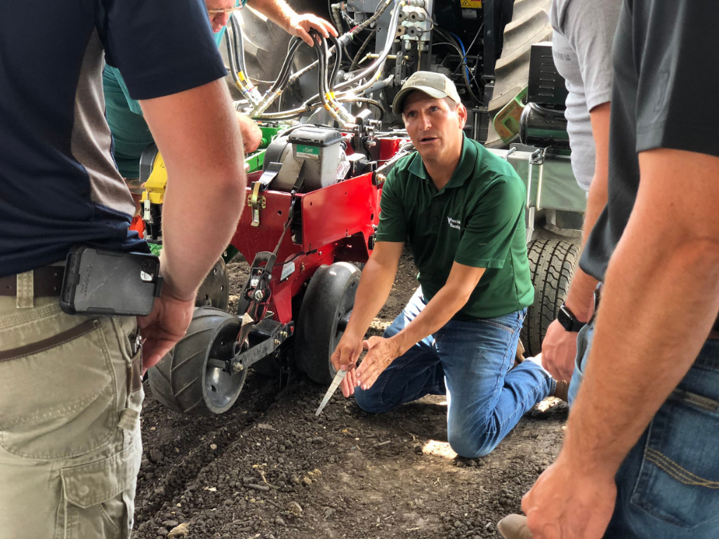 An agronomist shows PTI Farm Tour visitors how to check the furrow with a seed depth tool.