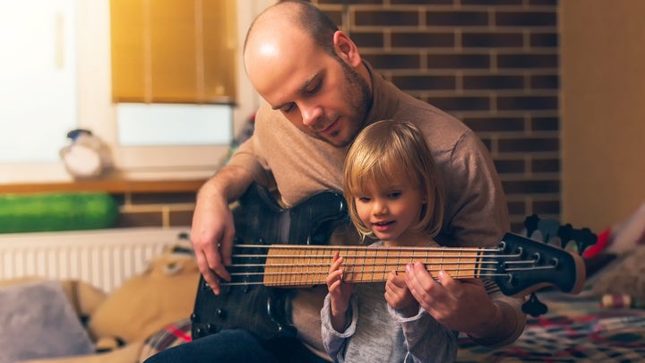 father playing bass and showing his toddler daughter how to play