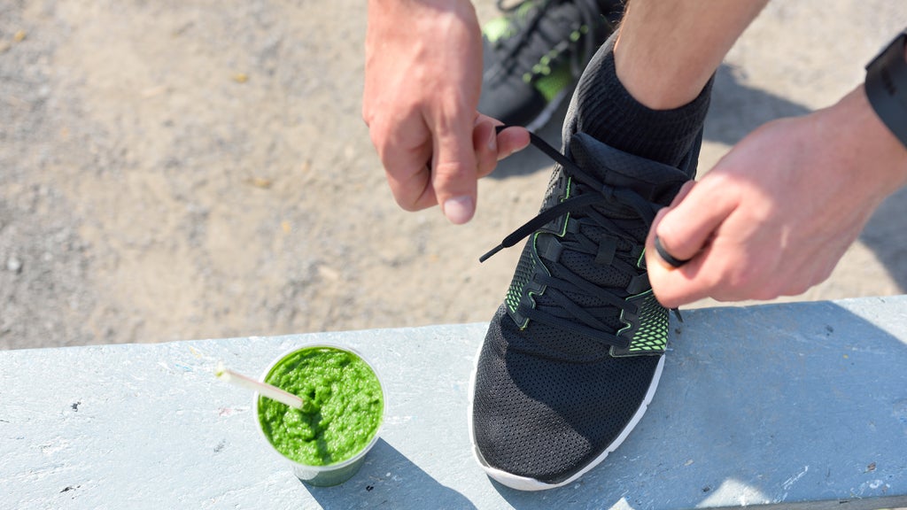Man tying his shoe before a morning walk with a green smoothie