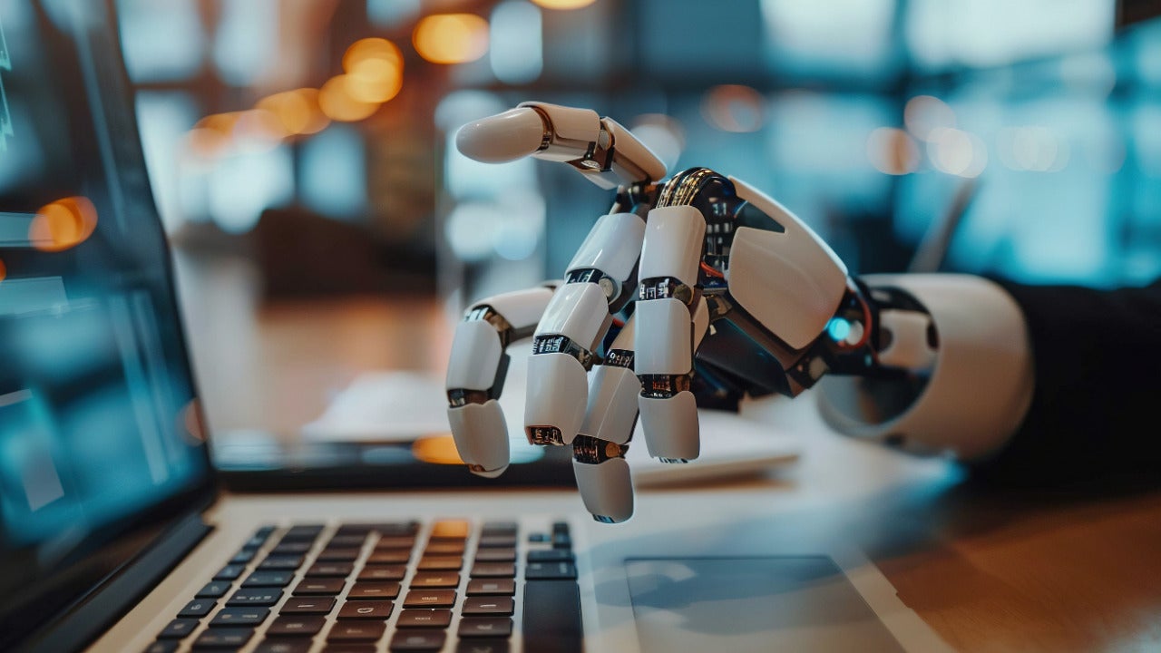 An image of a humanoid robot hand interacting with a laptop