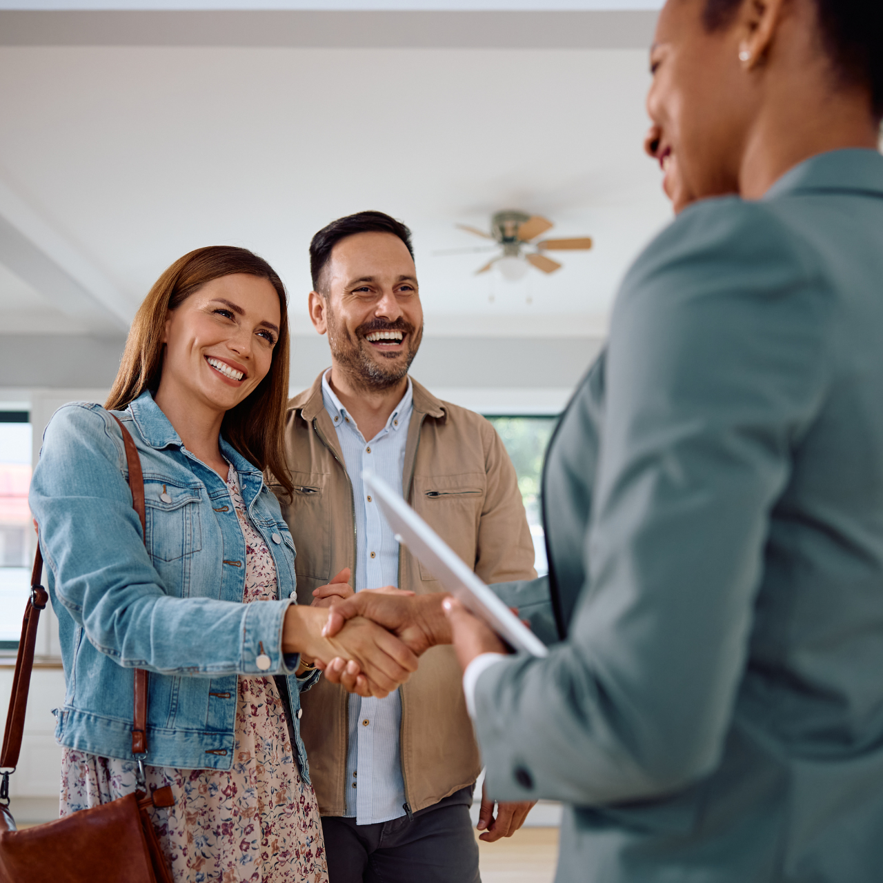A real estate agent is seen shaking hands with a couple. 