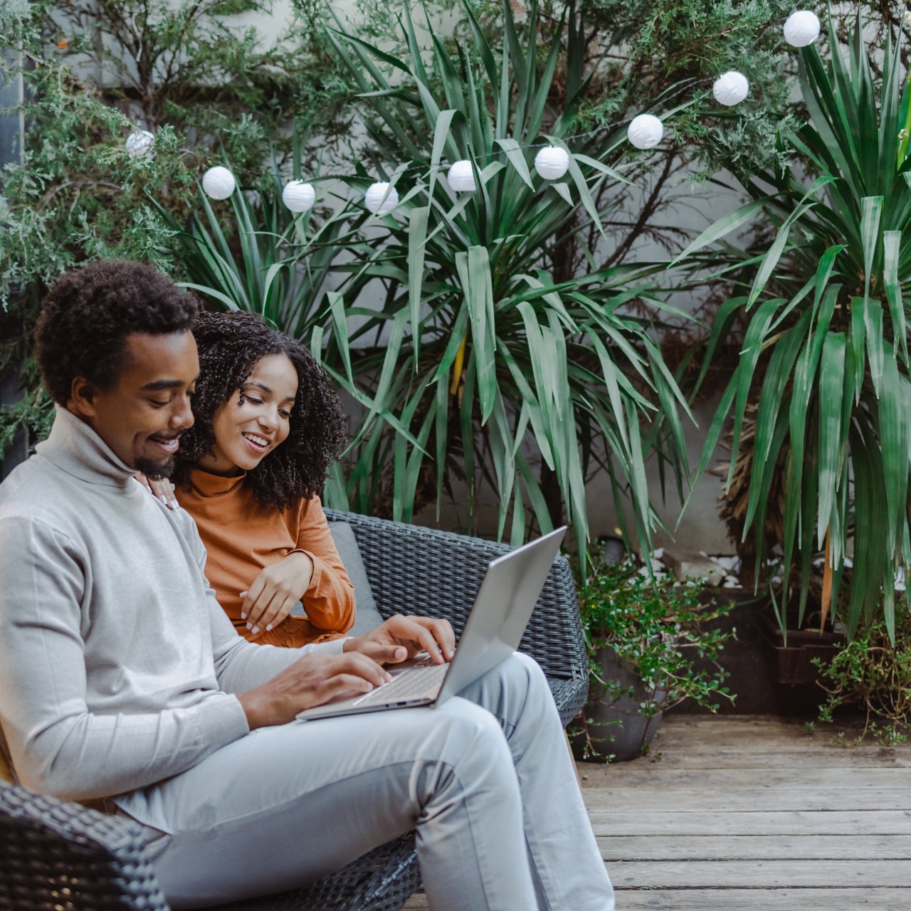A smiling couple on their back porch, using a laptop to compare prices and shop online for home services.