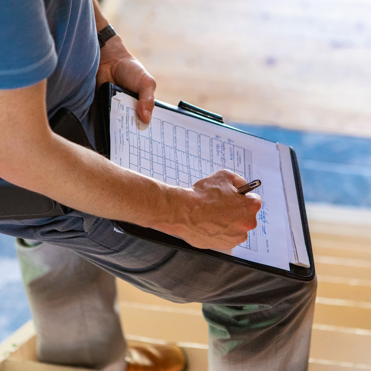 Someone is standing on staircase working on a paper with pen in his hand. He has kept the paper on his thigh for support.