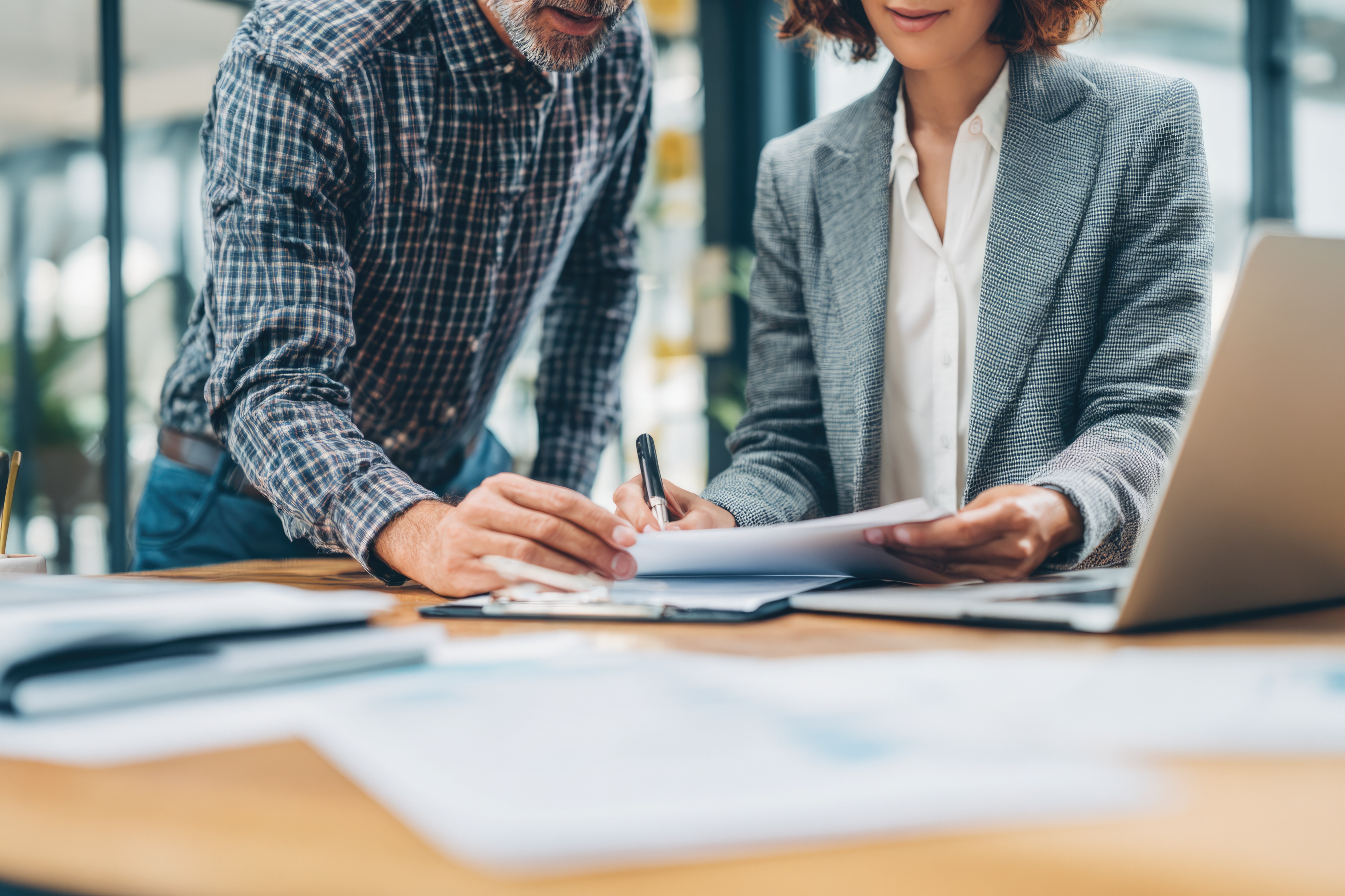 Two businesspeople looking at a document with an open laptop they're using to plan.