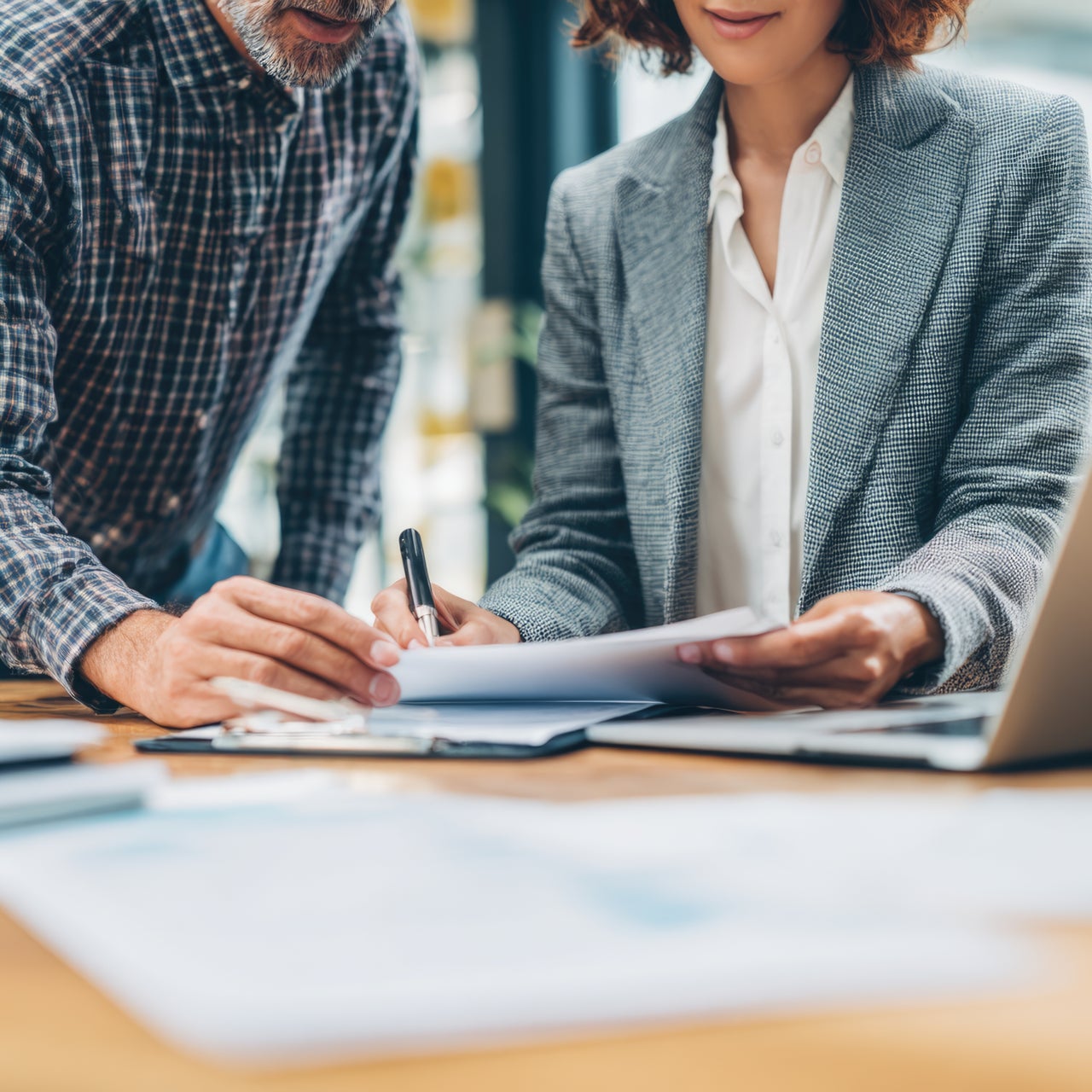 Two businesspeople looking at a document with an open laptop they're using to plan.
