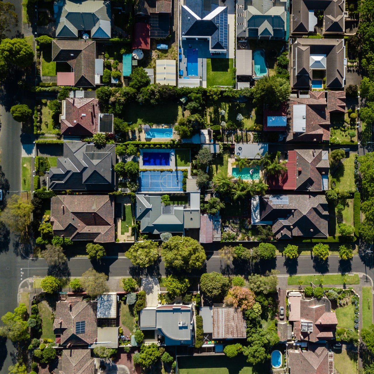 Residential area with several houses with varying roof styles and colors, interspersed with trees and patches of green lawns.
