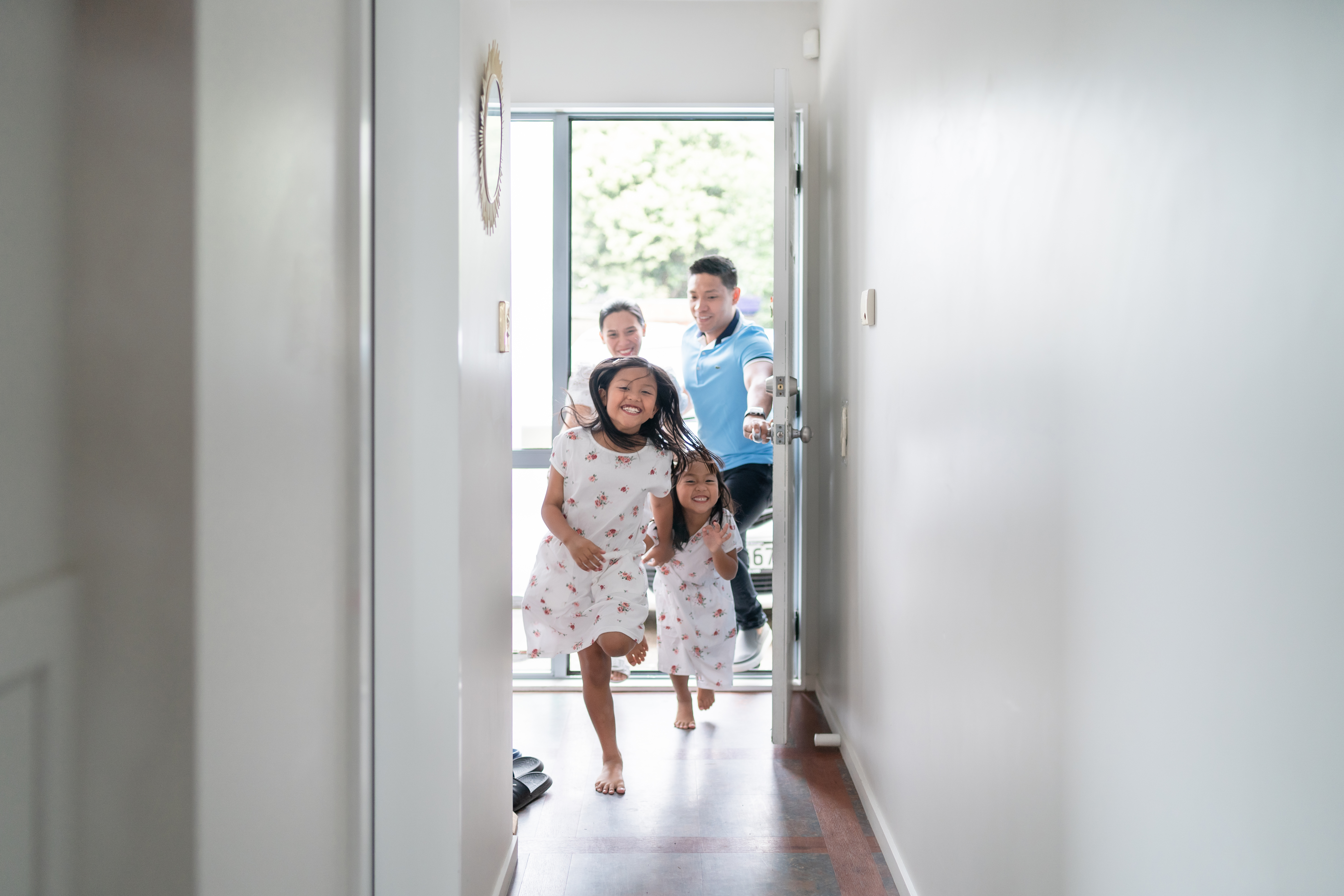 Two baby girls entering happily into a house while their father is holding the door open accompanied by the mother.