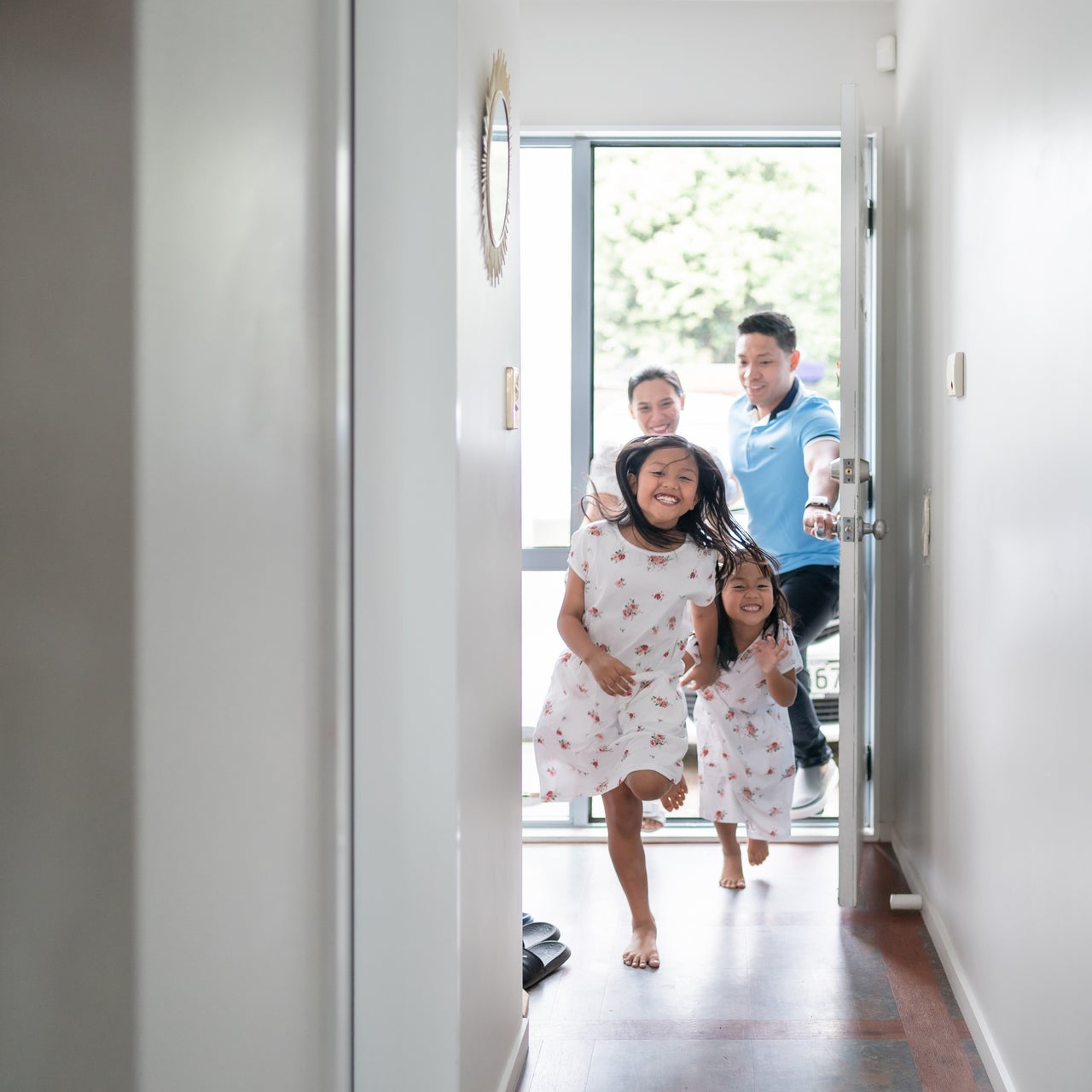 Two baby girls entering happily into a house while their father is holding the door open accompanied by the mother.