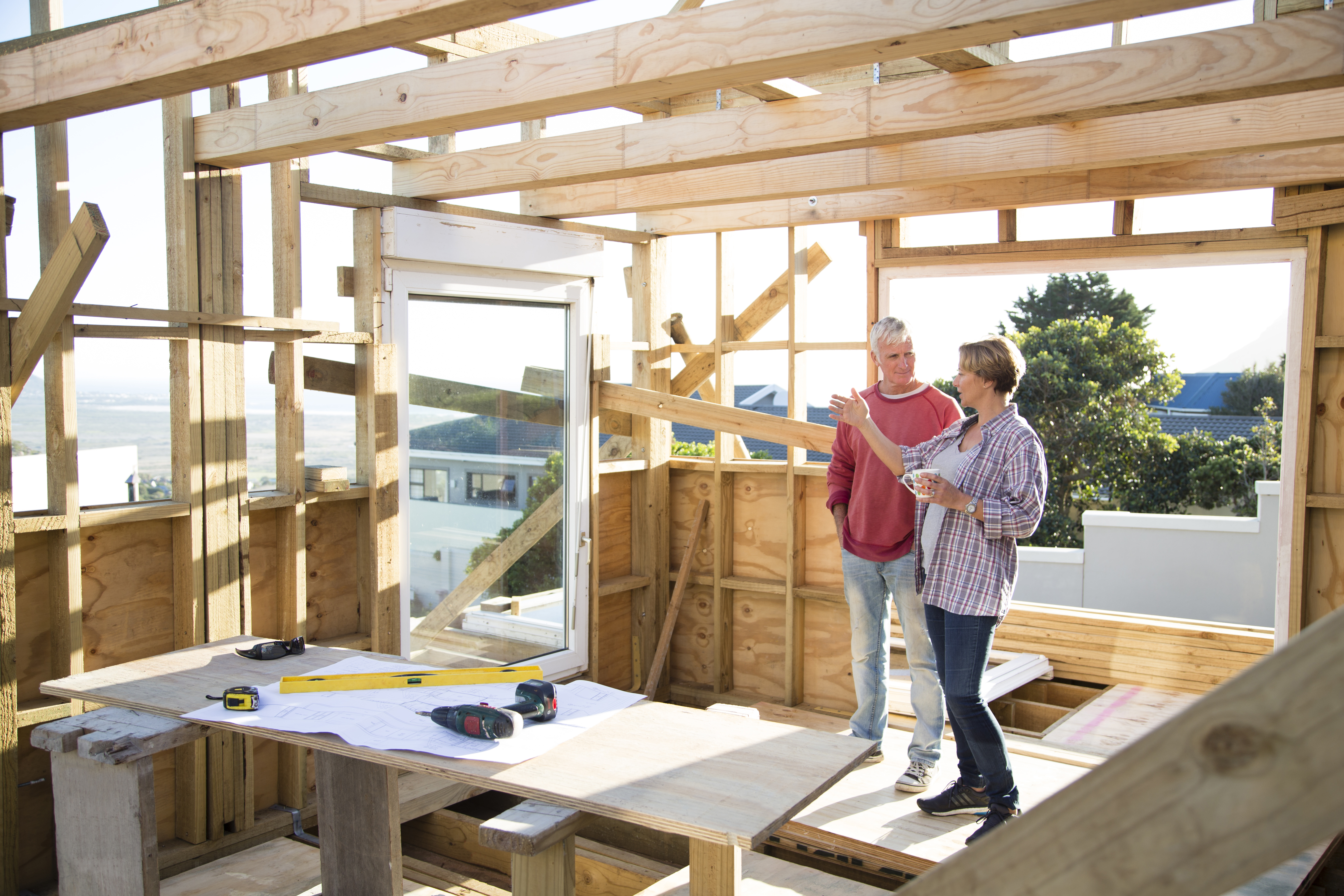 A male and a female, possibly a couple, discussing something about their wooden house under construction.