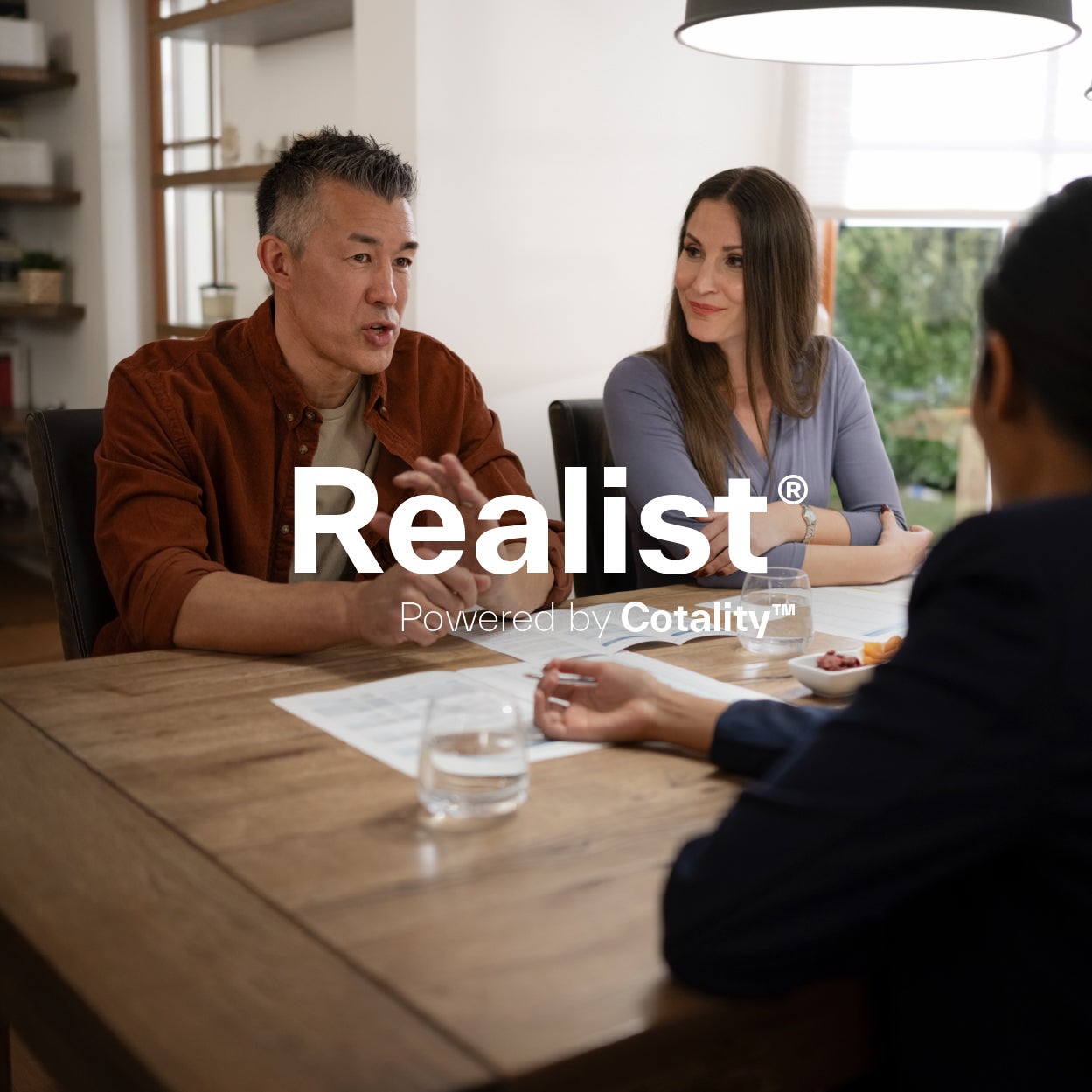 A business meeting with three people sitting around a wooden table. The text "Realist Powered by Cotality" is superimposed in the image.