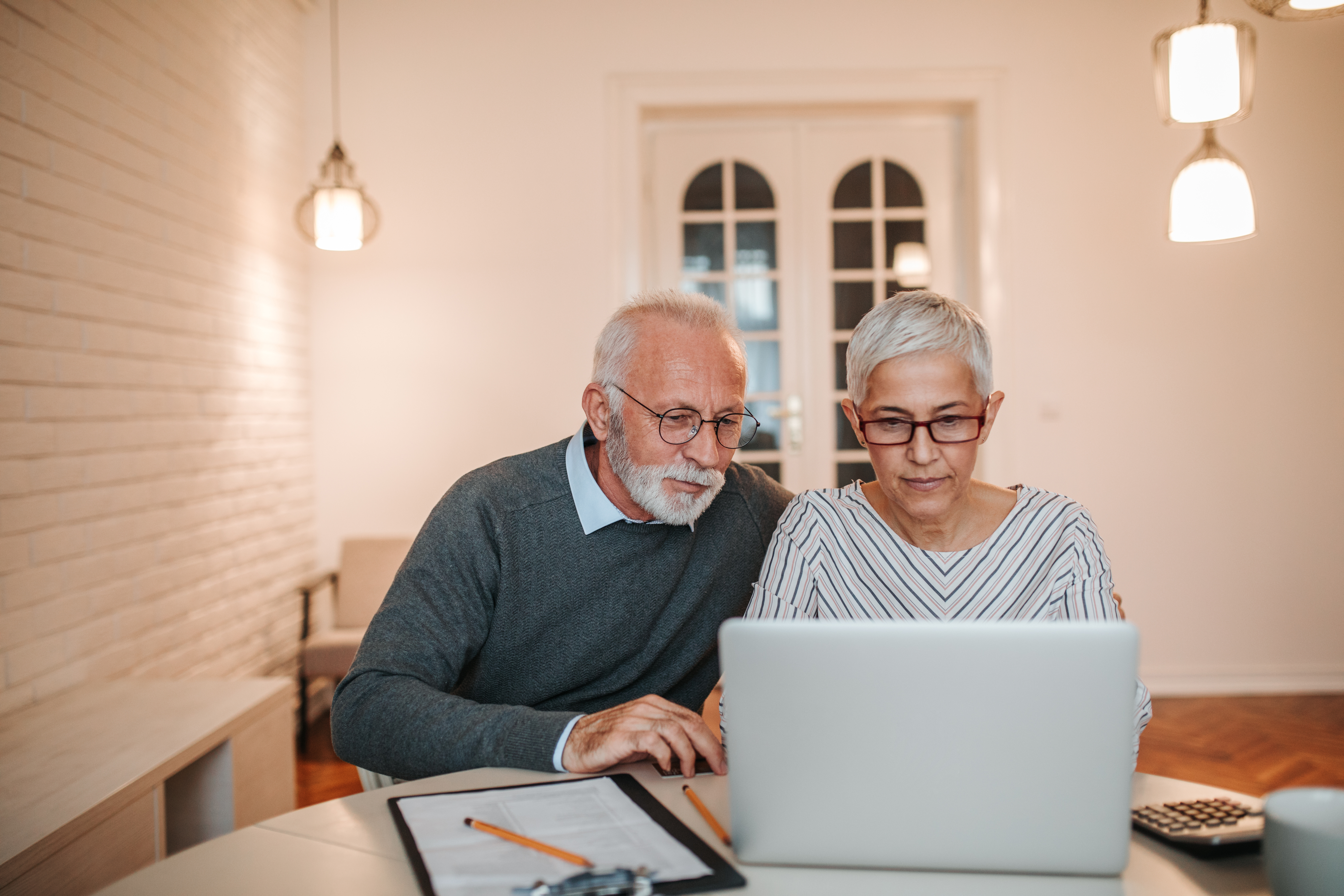 An elderly couple working together on their laptop kept on a desk.