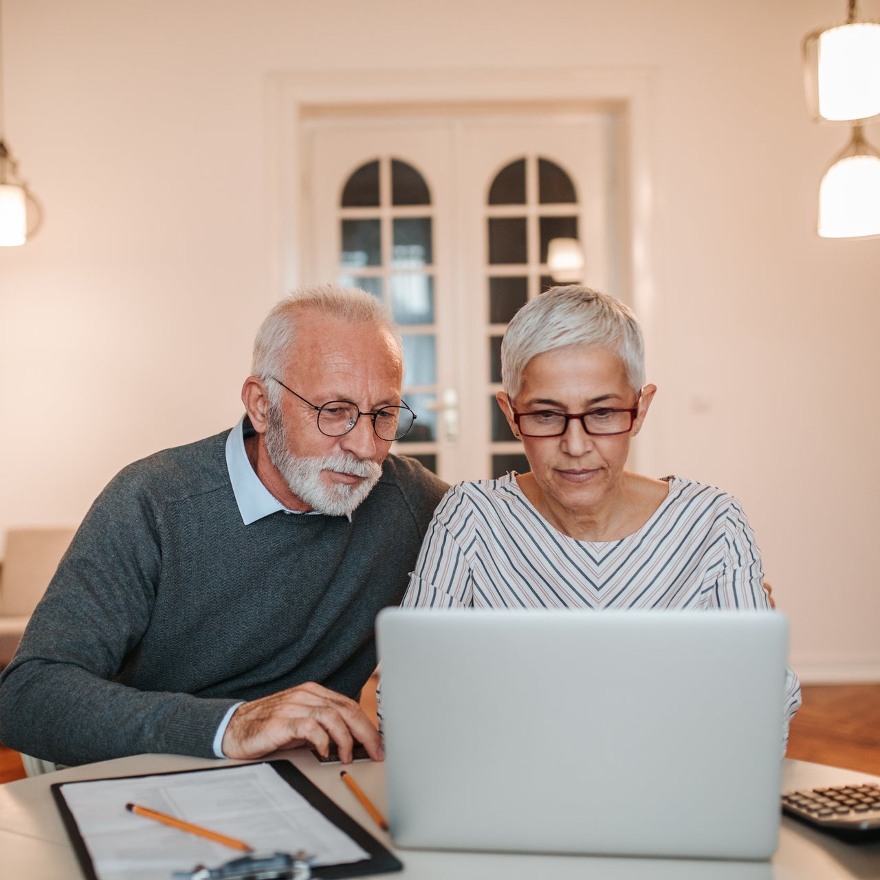 An elderly couple working together on their laptop kept on a desk.