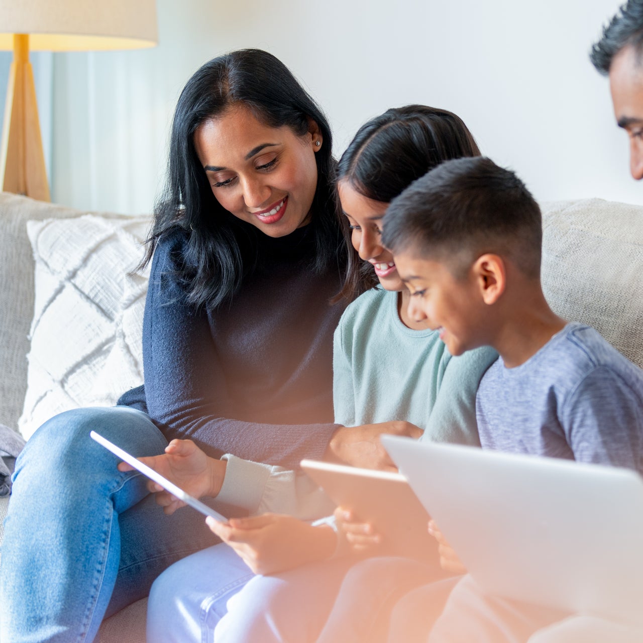 Two parents and two children on a couch in their house smiling while looking at a laptop and tablet.
