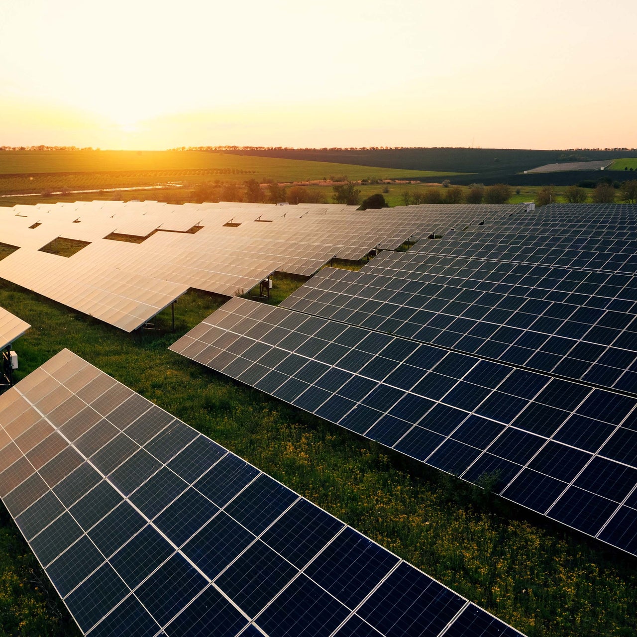 A view of numerous solar panels on the top of a property. An engineer is seen walking through it.