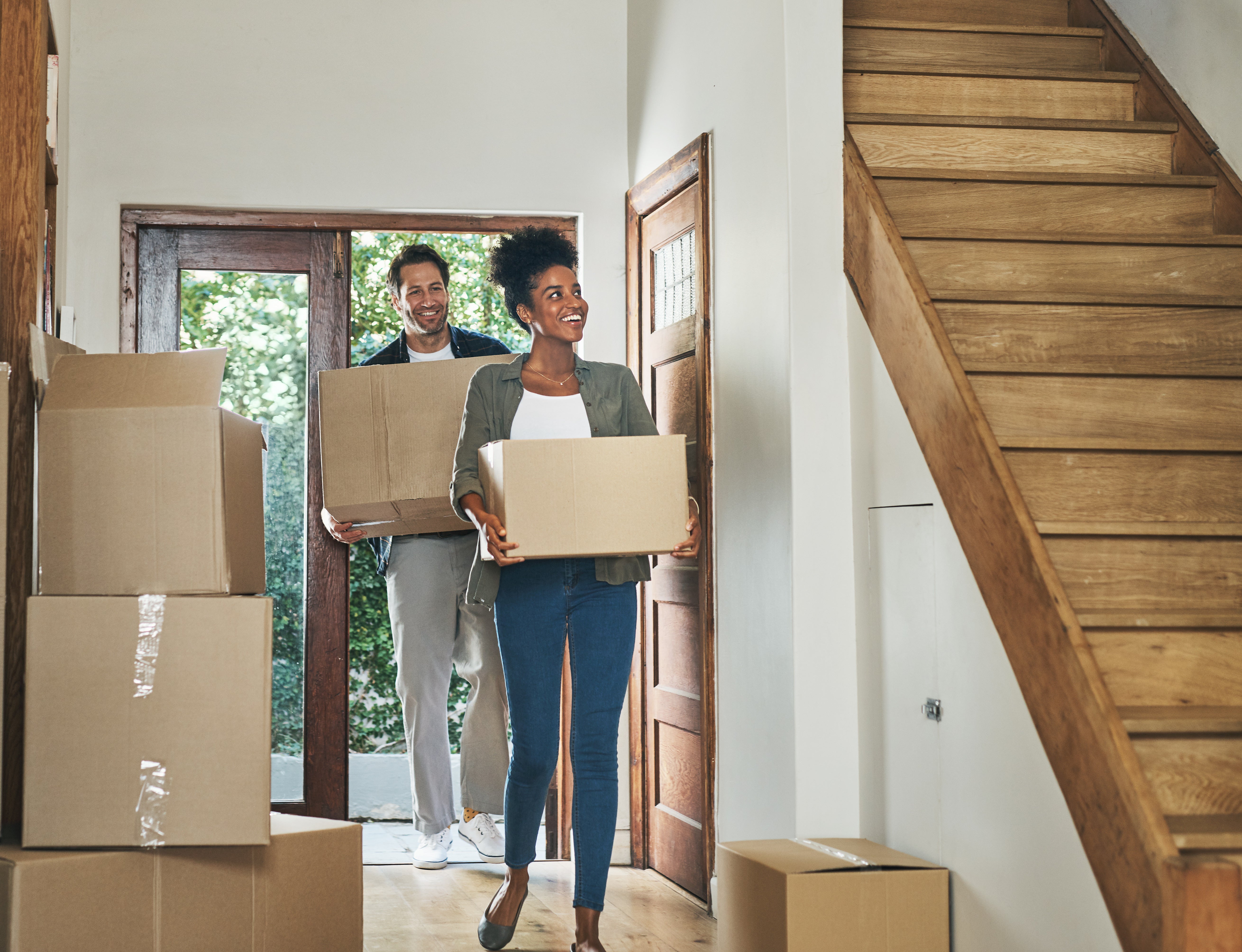 Couple moving into a new modern house, carrying boxes and arriving home together. 