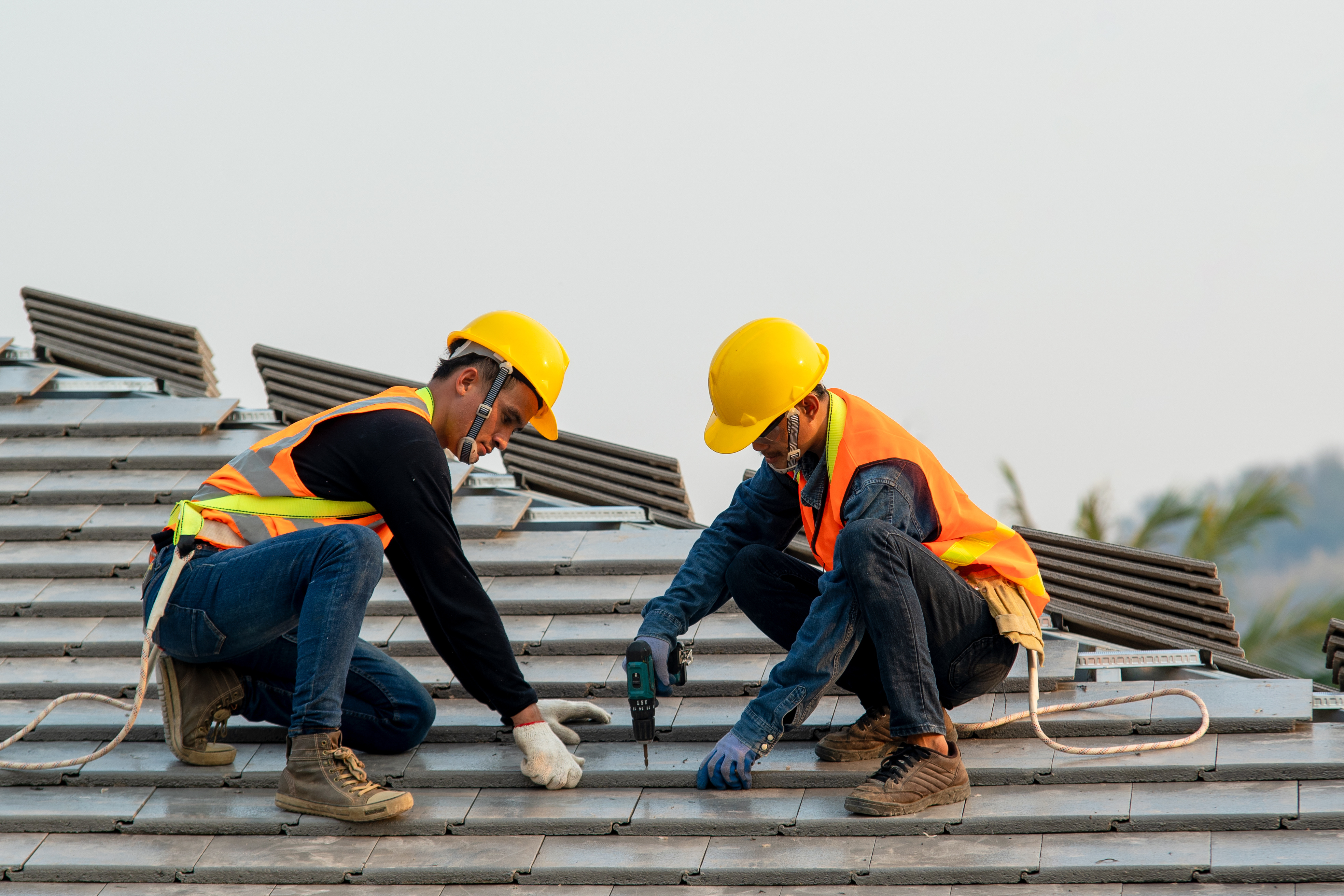 Two construction workers are installing roofing tiles on a rooftop. 