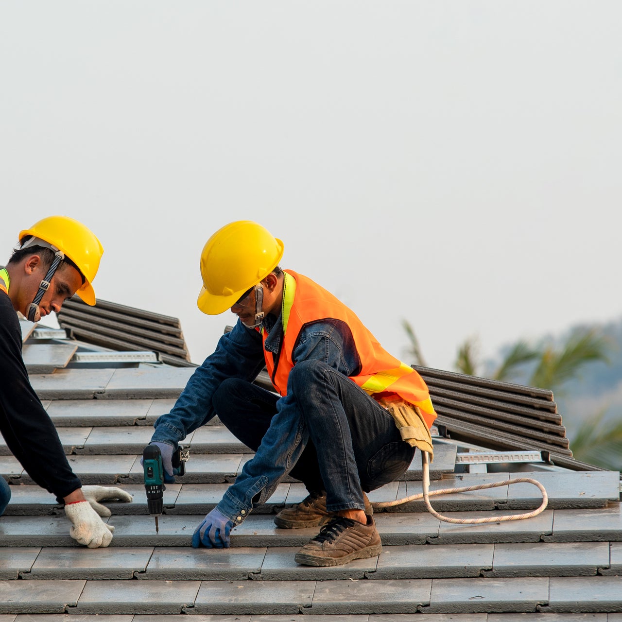 Two construction workers are installing roofing tiles on a rooftop.