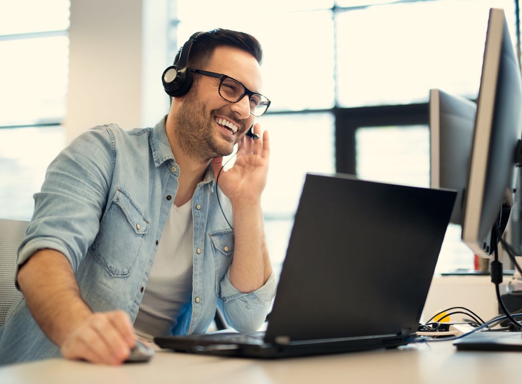 Man with headset at laptop, smiling.