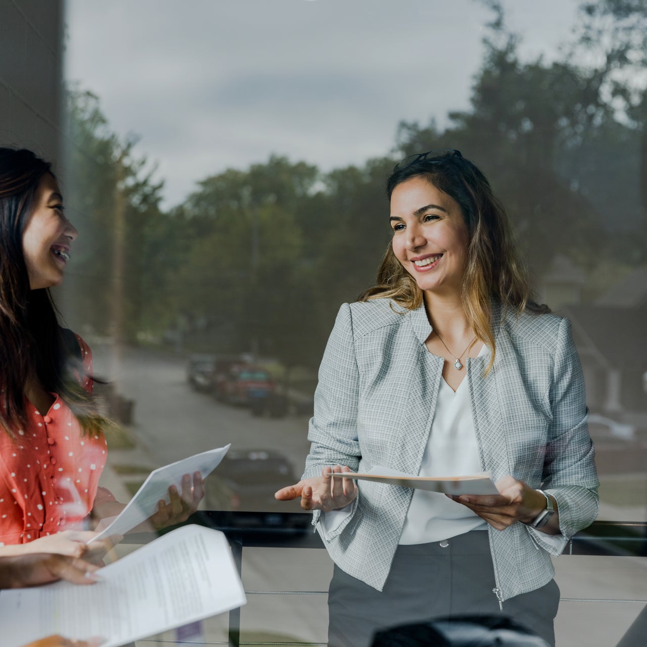 Two women smiling at each other while holding some papers in their hands.
