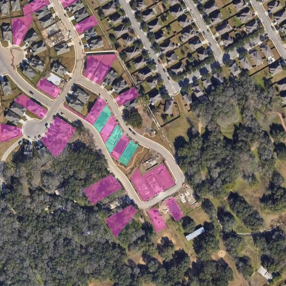 An aerial view of a residential development area, where some lots are highlighted in pink and green.