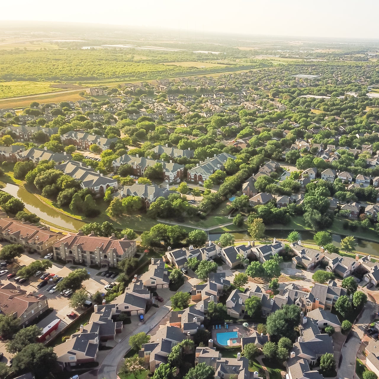 Aerial view of a suburban neighborhood with houses, streets, trees, and a swimming pool.