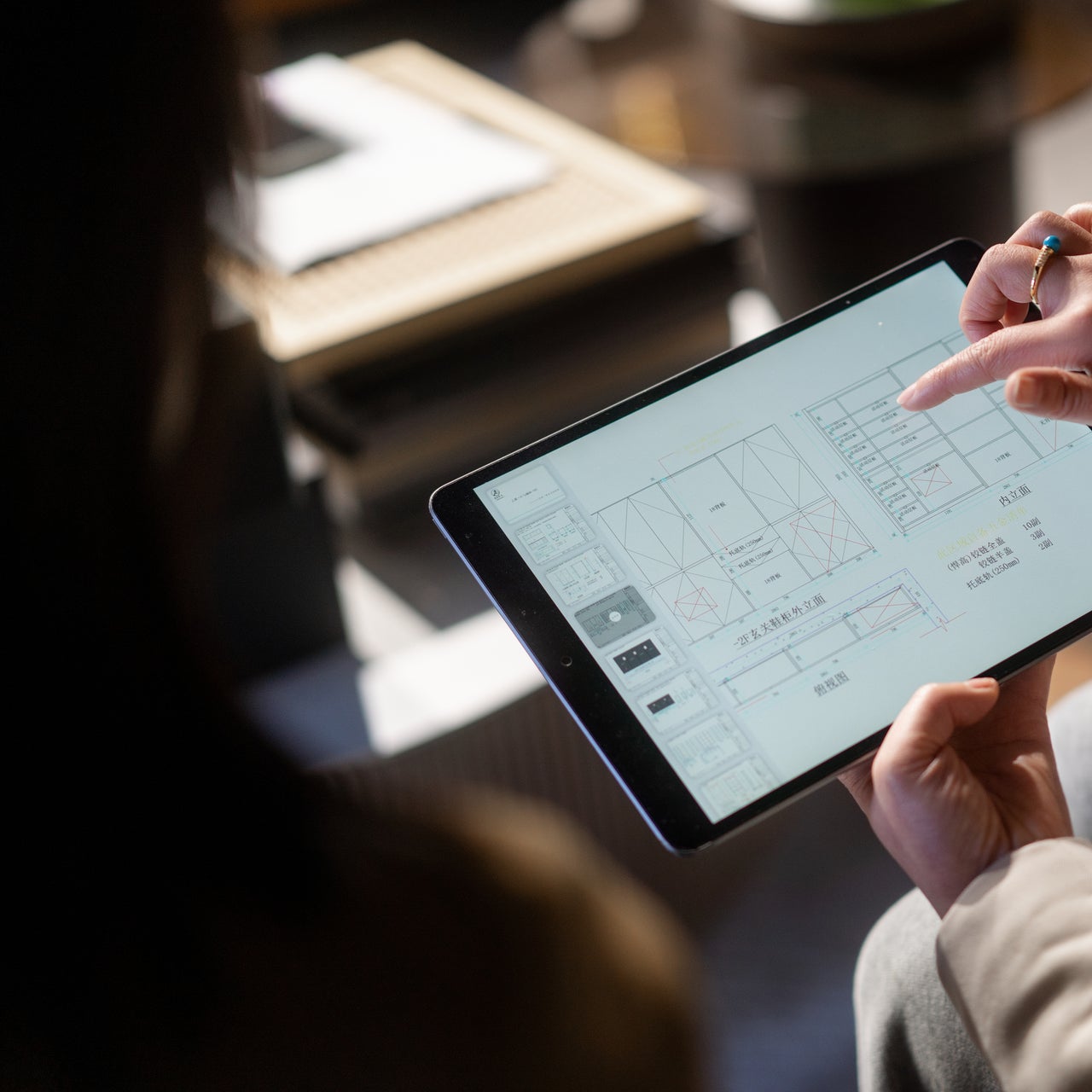A hand of a man is visible working on a blueprint of a plan on a tablet.
